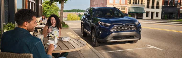 2025-Toyota-RAV4-parked-next-to-a-cafe-with-a-couple-dining-and-smiling