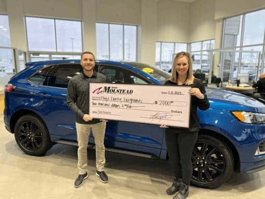 Two people holding a check in front of a vehicle
