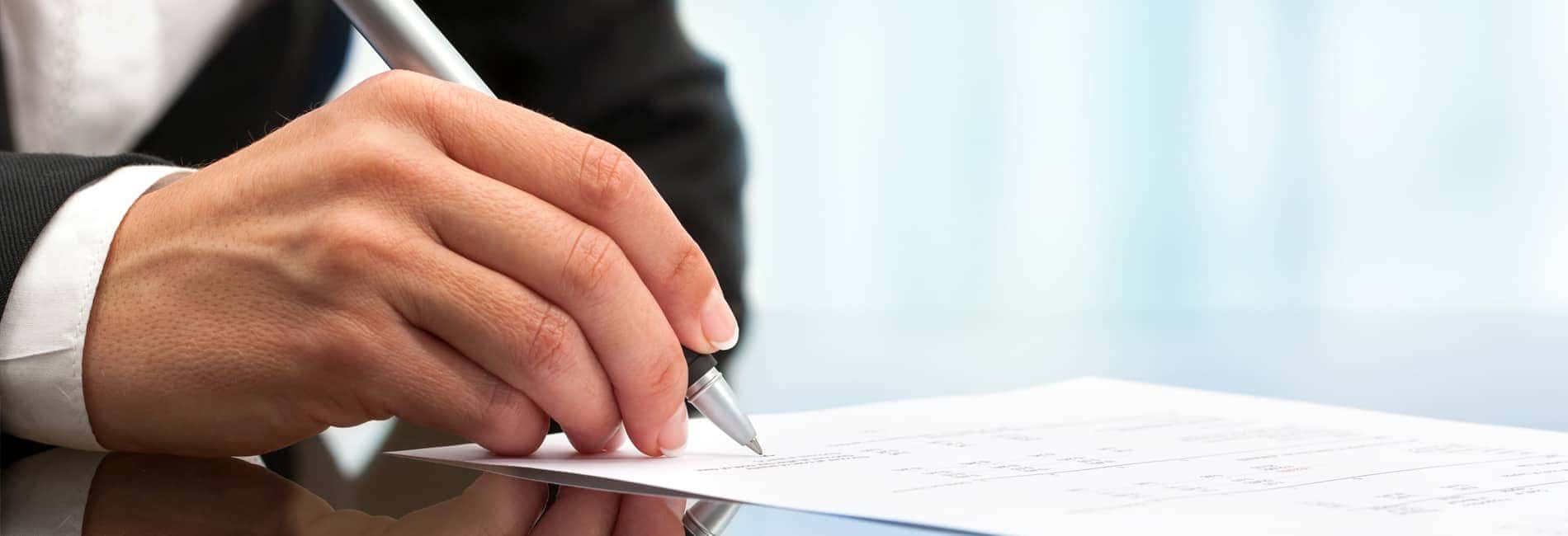 a man's hand signing paperwork on glass table