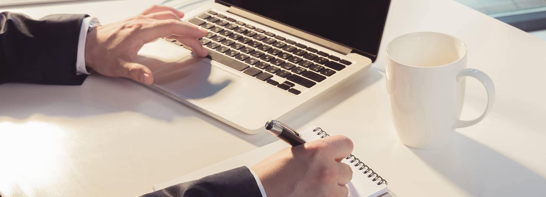 Hand pressing spacebar on a laptop while writing a note on a notepad
