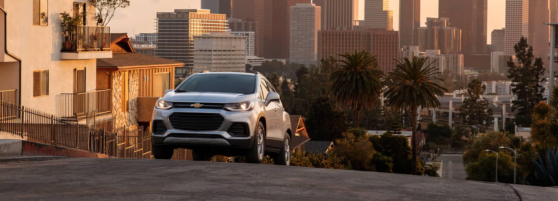 A silver 2021 Chevrolet Trax driving up a city hill at sunset