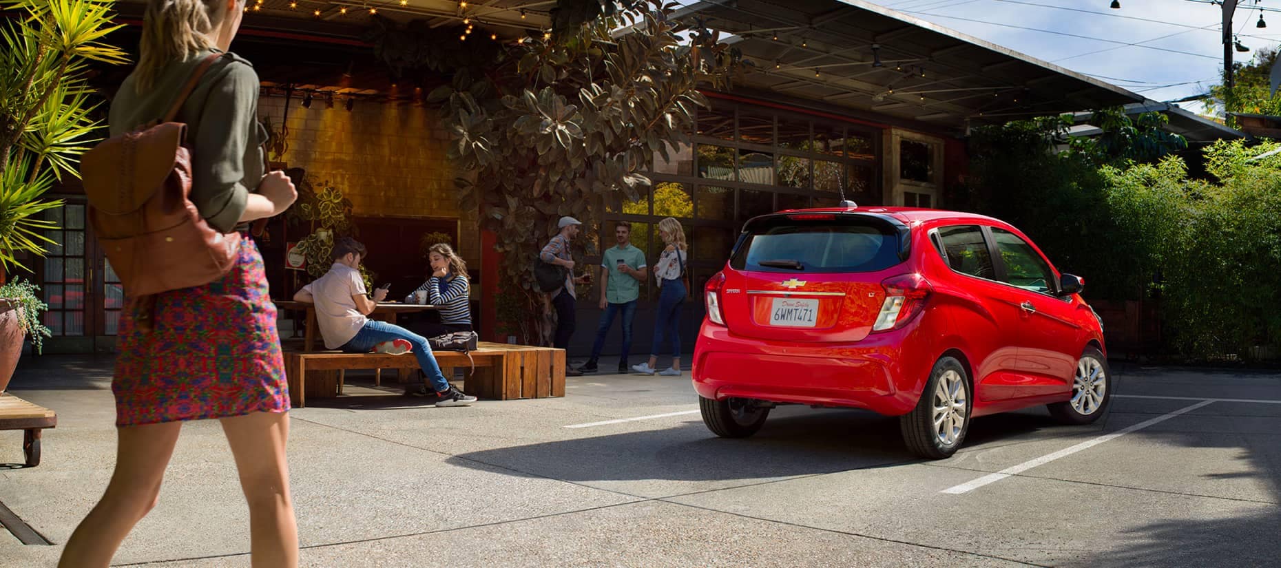 Woman walks past a red Chevy spark parked at a restuarant.