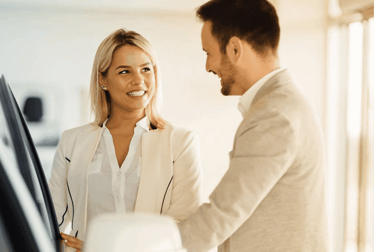 car salesman shows happy woman car in showroom 