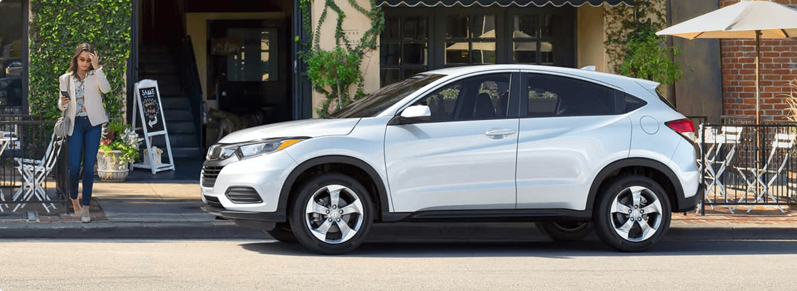 woman waits on sidewalk next to parked Honda