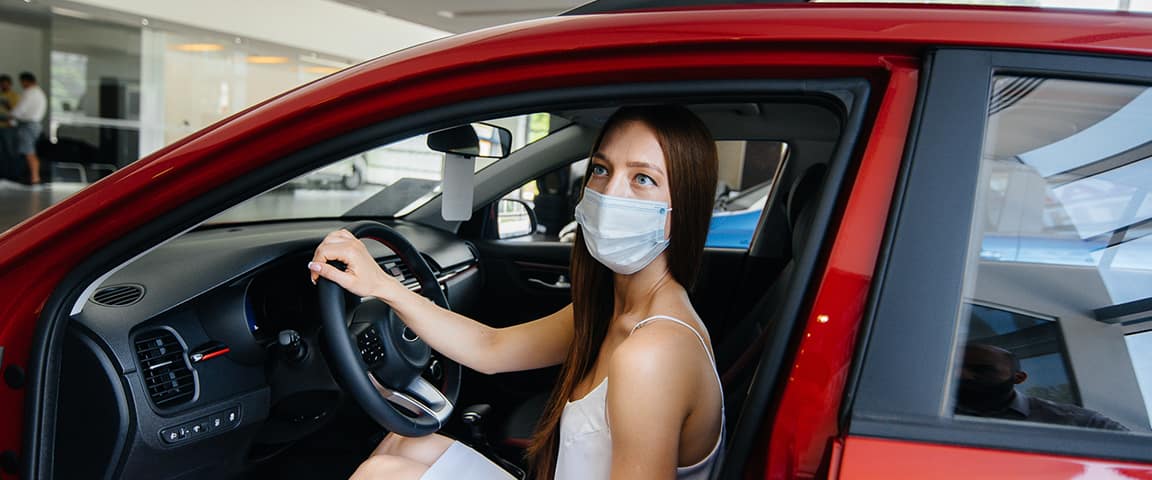 woman with mask sits in showroom car
