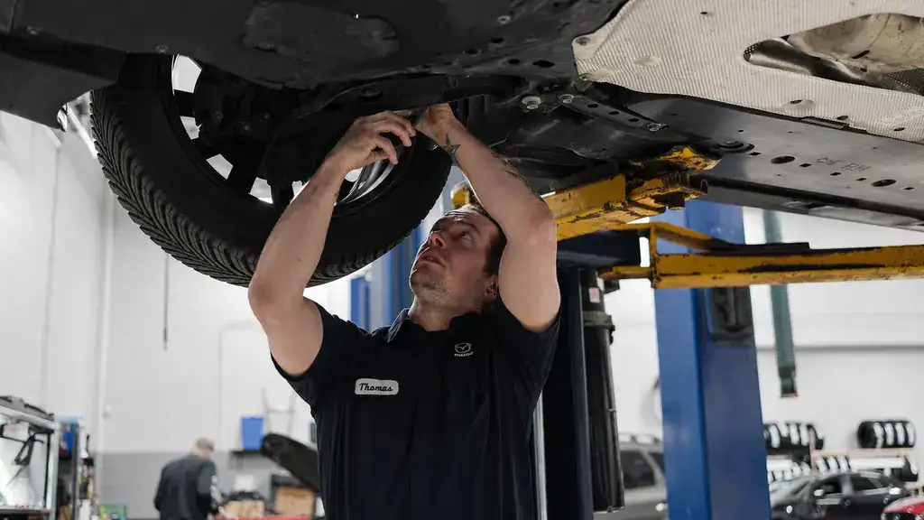 Mazda technician performing undercar service on a vehicle raised on a lift