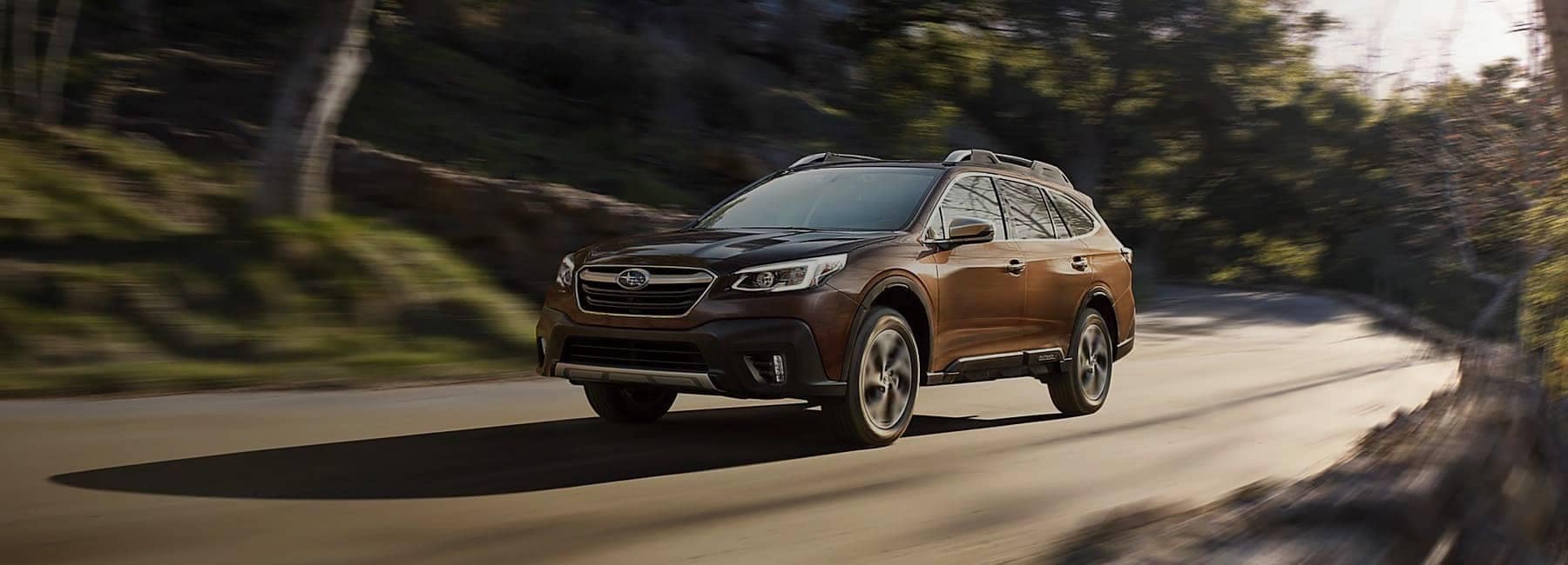 2022 Subaru Outback in Brown Pearl side three-quarter view driving down forest road