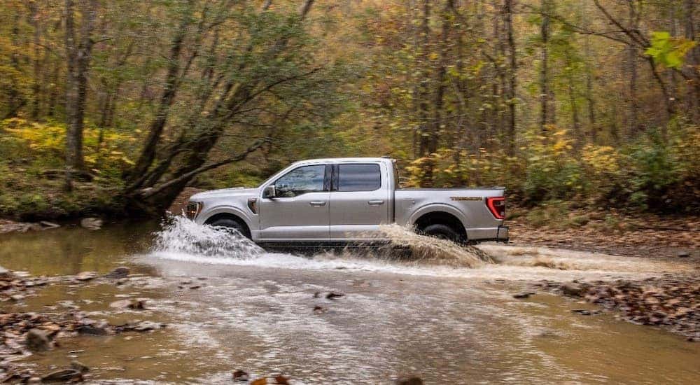A silver 2021 Ford F-150 Tremor is shown from the side splashing through a creek.