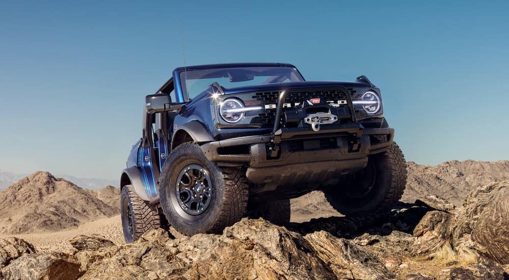 A blue 2021 Ford Bronco 4 door is shown from a low angle parked on rocky terrain with no doors.