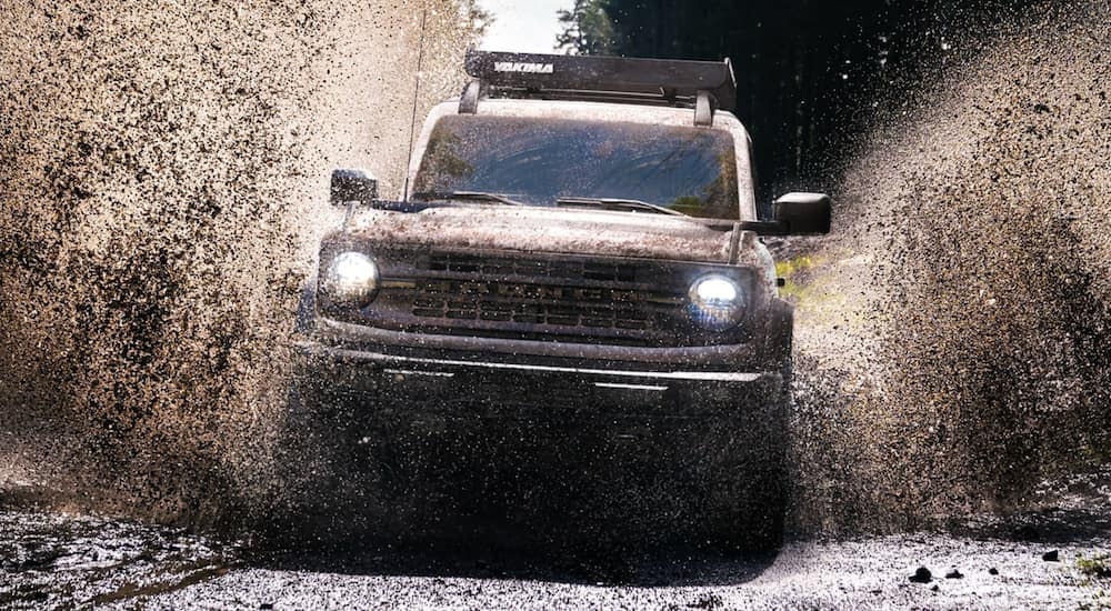 A white 2021 Ford Bronco is shown from the front off-roading through a puddle after leaving a Tennessee Ford dealer