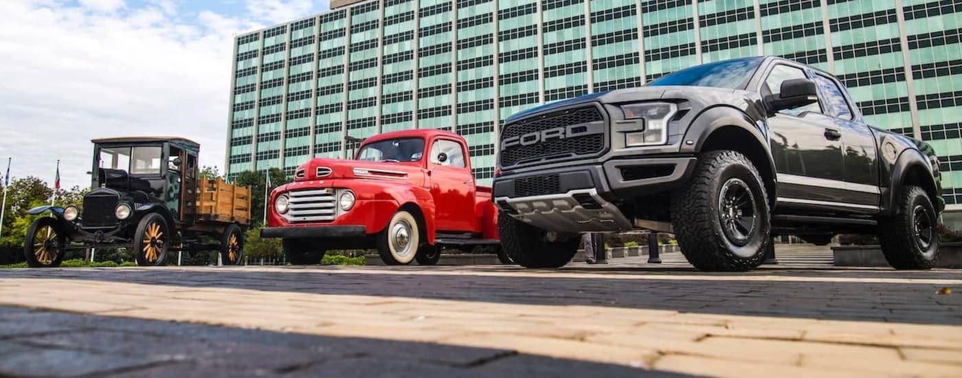 A 1917 Model TT, a red antique pickup, and a black 2017 Ford Raptor are parked in front of an office building.