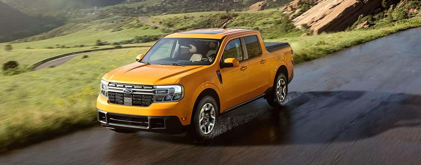 A yellow 2022 Ford Maverick is shown from the front driving on an open road after leaving a Lynchburg Ford dealership.