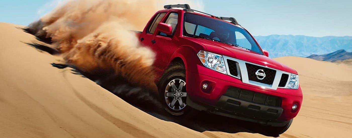 A red 2021 Nissan Frontier is kicking up sand in a dune.