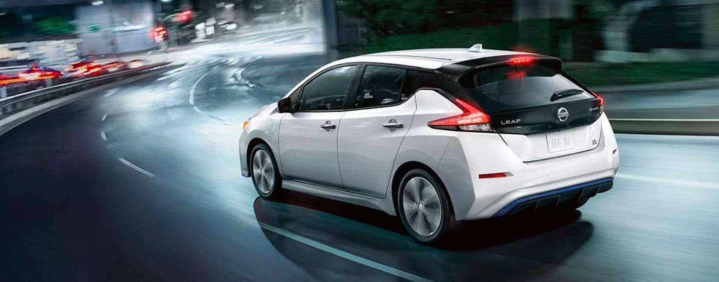 A white 2021 Nissan Leaf is shown from the rear and angled while driving on a highway at night.