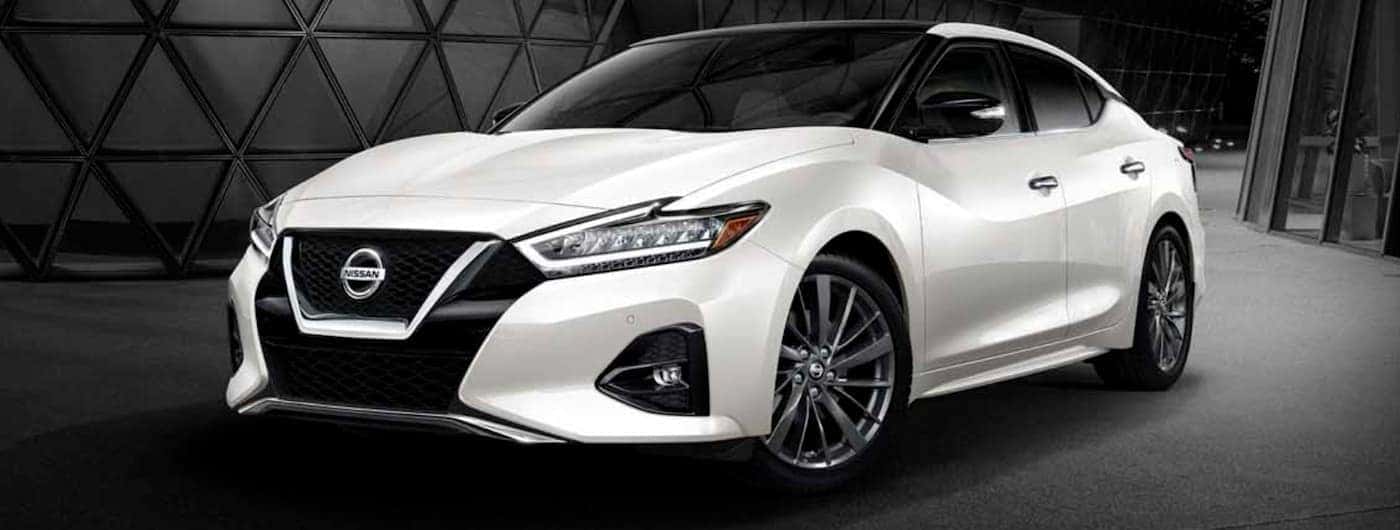 A white 2019 Nissan Maxima is in front of a dark building.