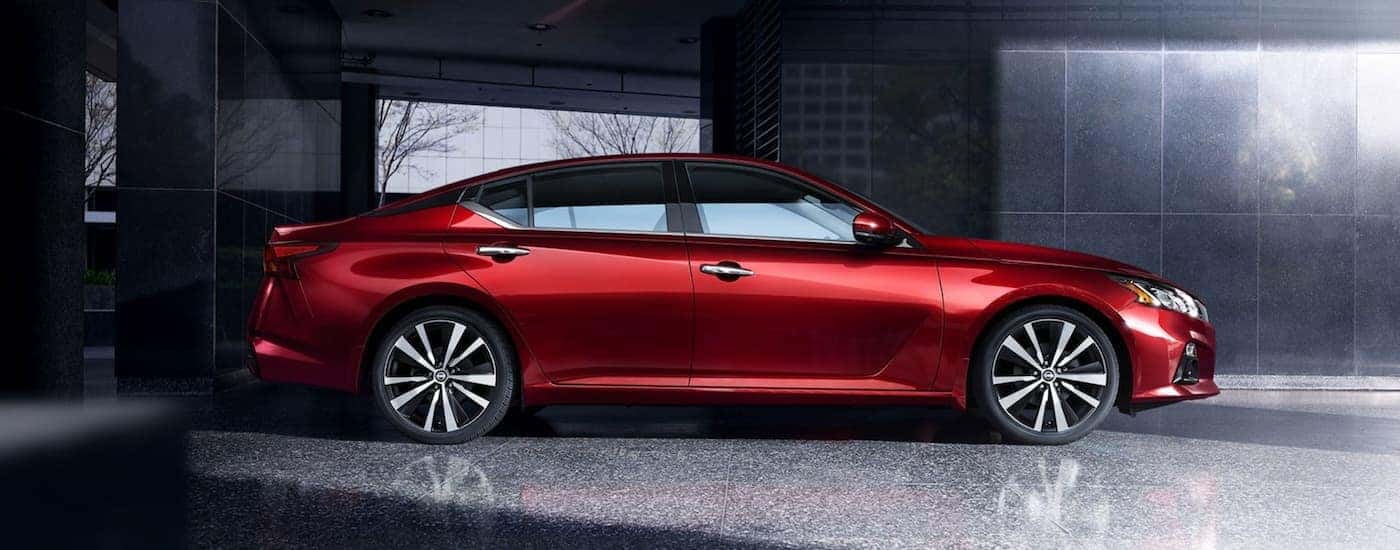 A red 2020 Nissan Altima is shown from the side in front of a grey building.