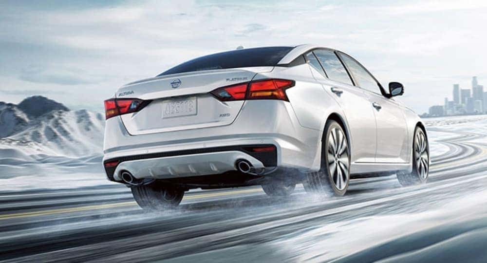 A white 2020 Nissan Altima is driving on a snowy road.