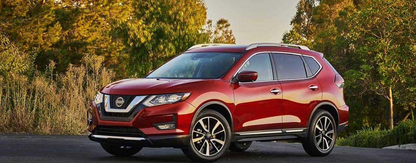 A red 2020 Nissan Rogue is parked in front of trees.