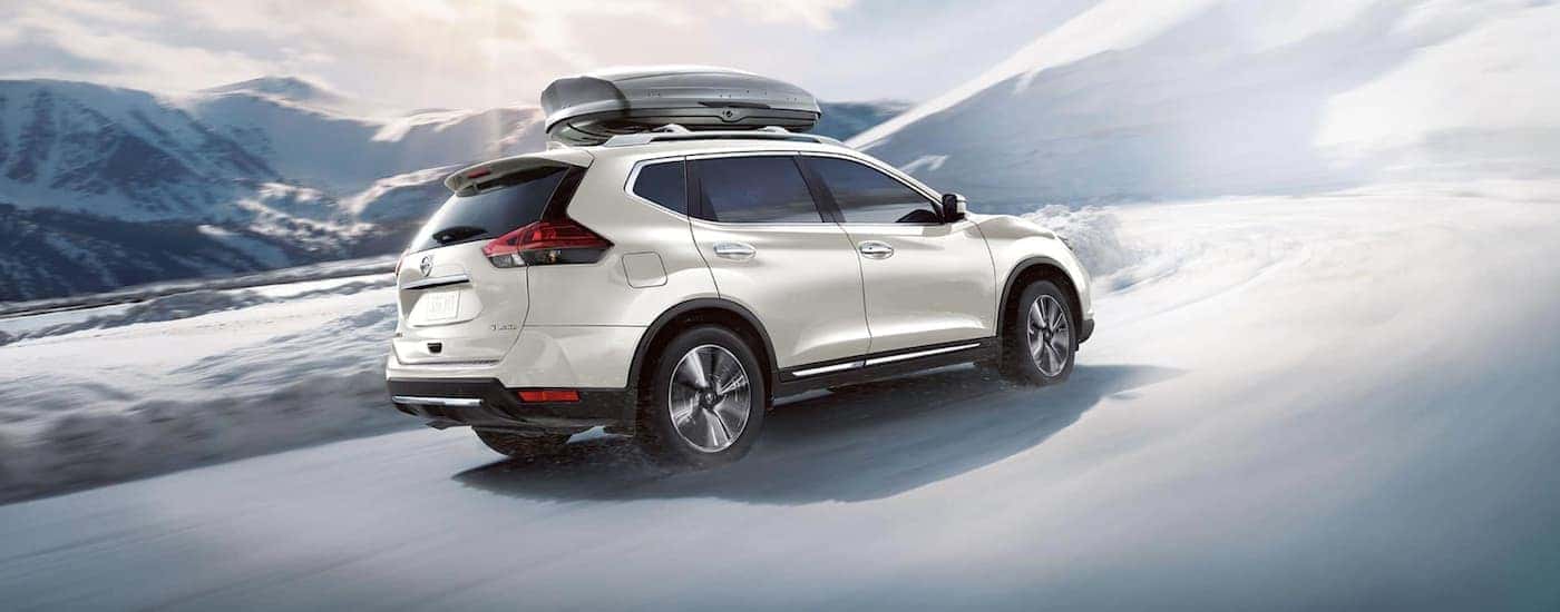 A white 2020 Nissan Rogue is driving on a snowy road.