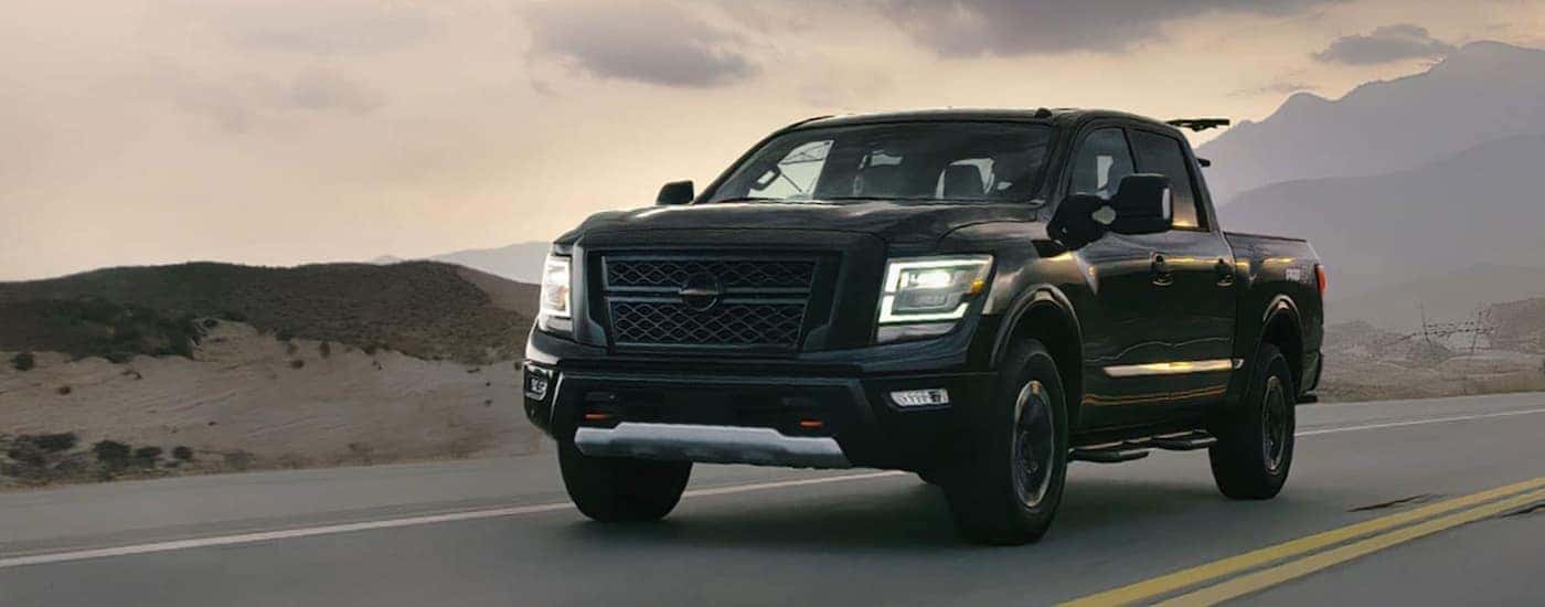 A black 2020 Nissan Titan is driving on a rural road at sunset.