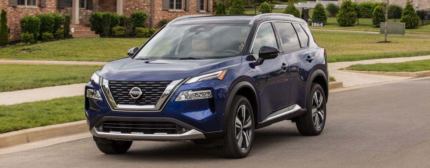 A blue 2021 Nissan Rogue is driving on a suburban road.