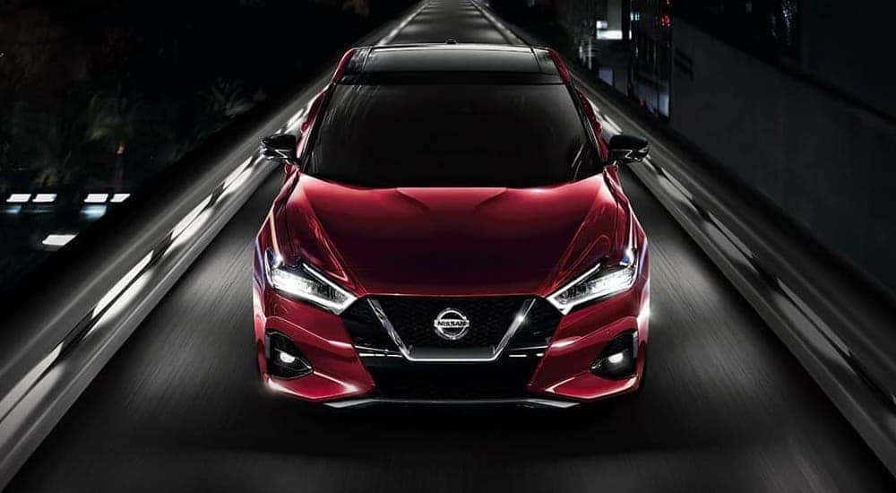 A red 2021 Nissan Maxima is shown from the front while driving on a narrow highway at night.