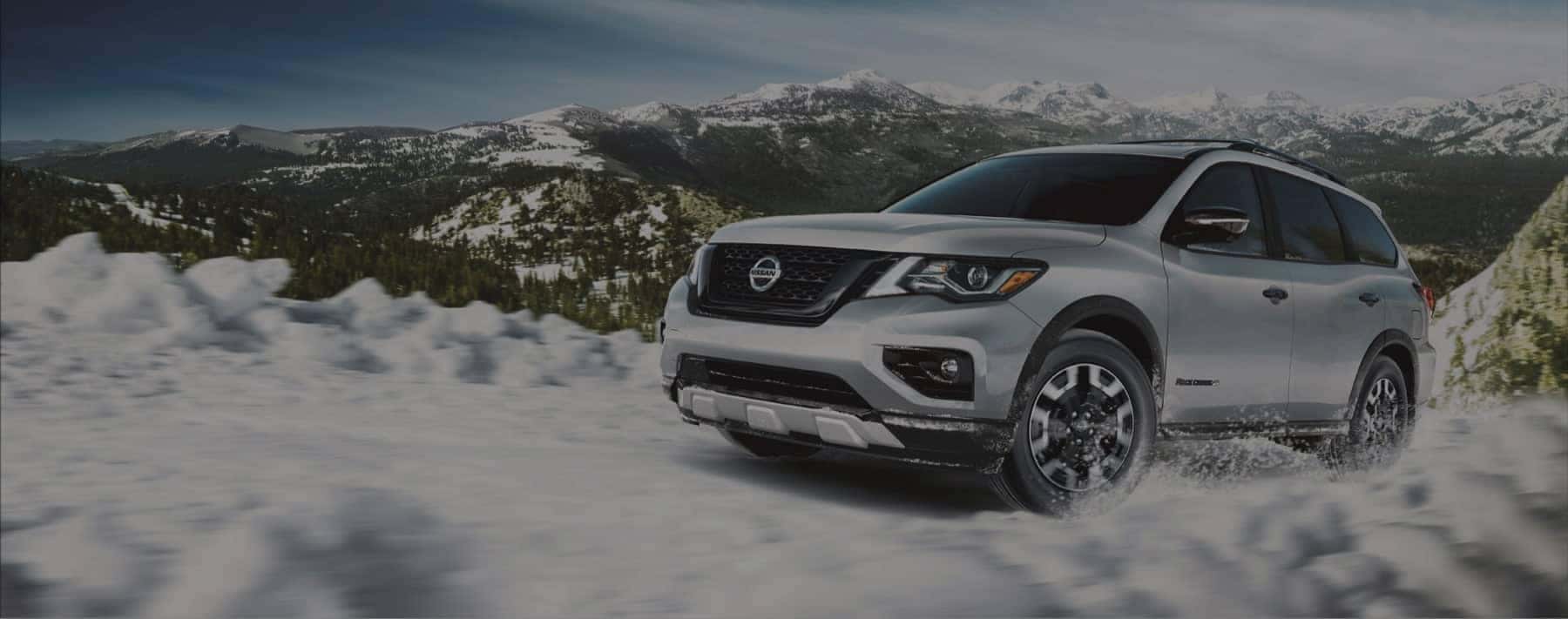 A silver Nissan SUV driving through a snowy mountain road.
