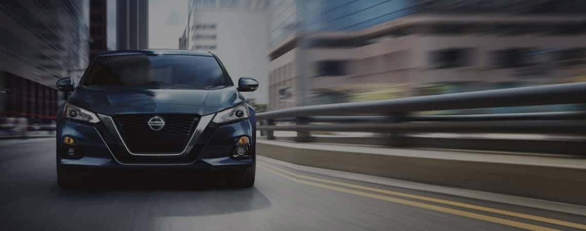 Head-on view of Nissan sedan driving through a city
