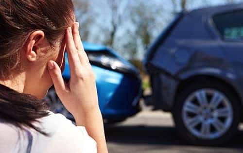 woman holding her head in hands looking over car crash