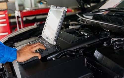 technician working on laptop at a car's open hood