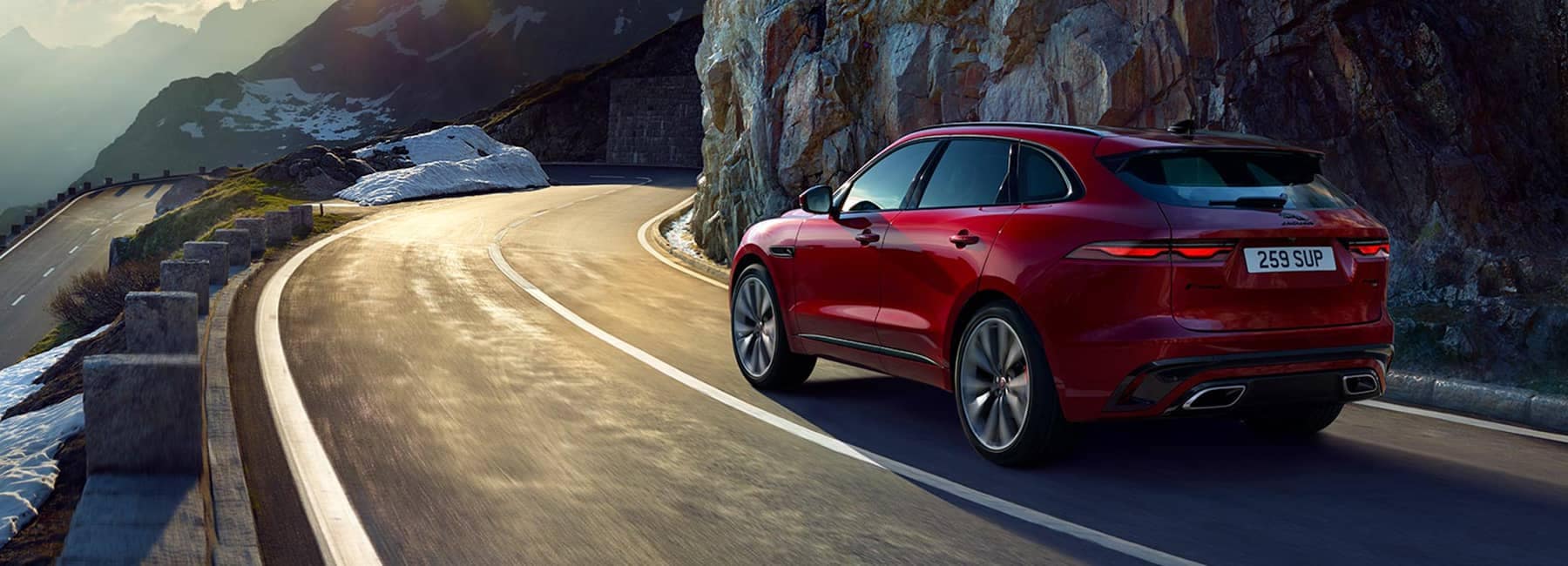 Red 2022 Jaguar F-Pace driving down road next to cliff