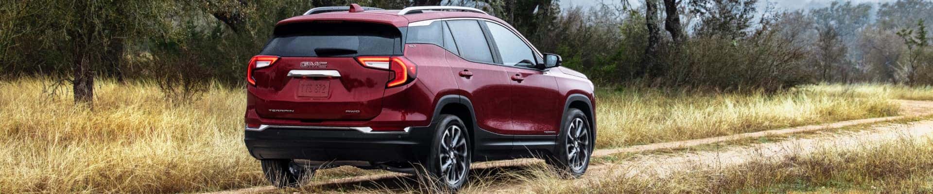 A red 2024 GMC Terrain SLT driving on a dirt path.