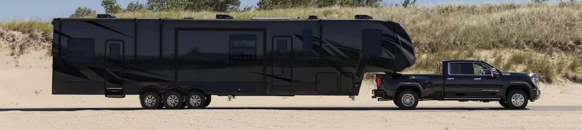 A black 2024 GMC Sierra 2500 HD towing a long trailer.
