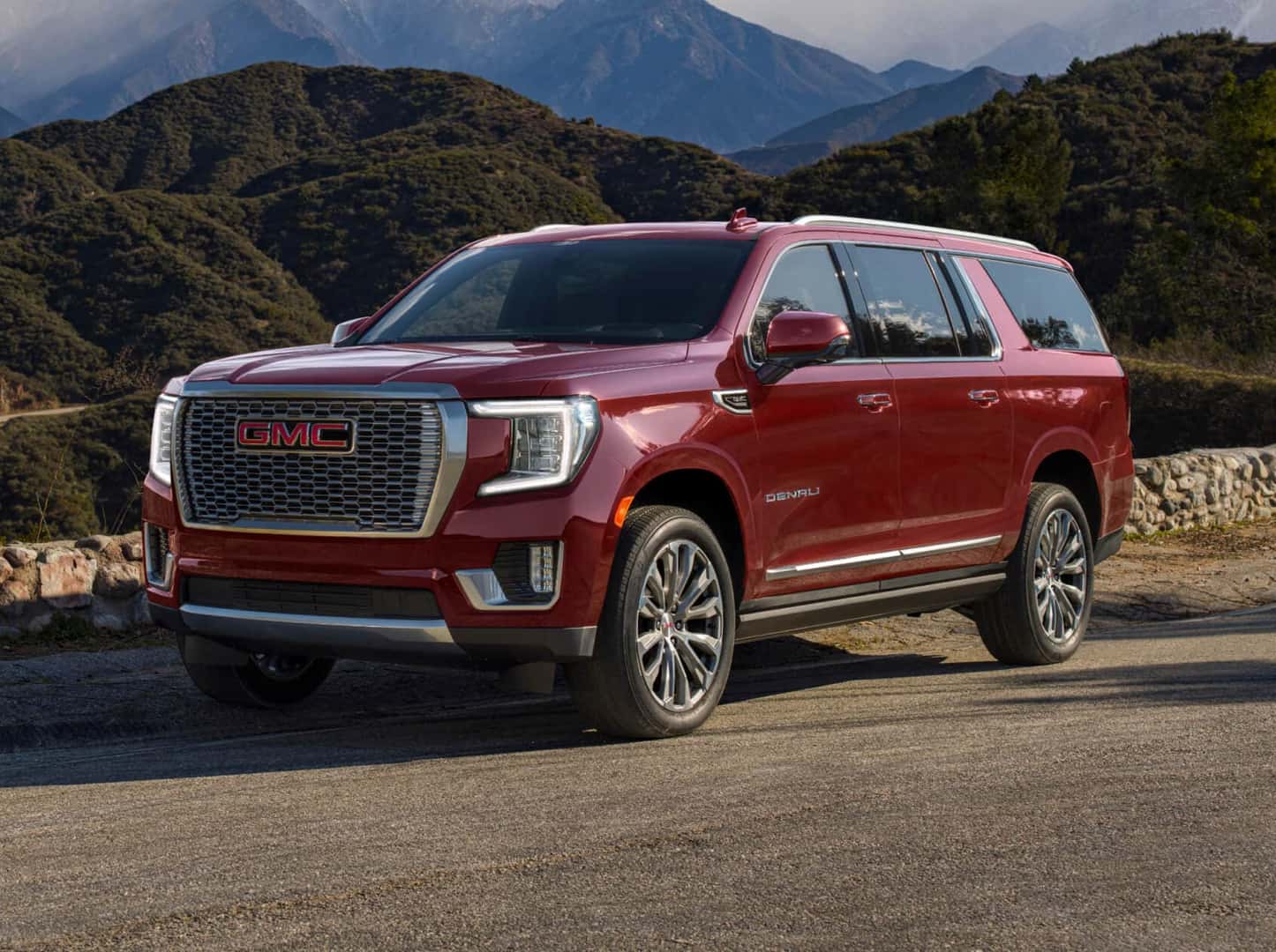 A red 2024 GMC Yukon XL parked near a stone wall.