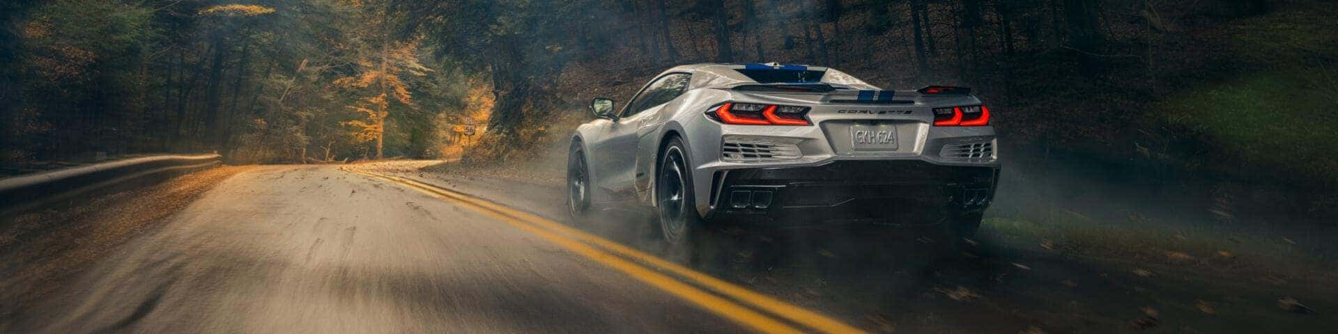 Silver Chevy Corvette driving on a winding pack road