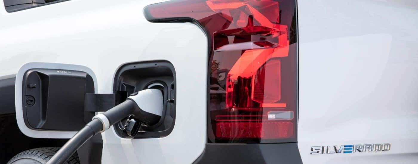 A close up shows a plug charging a white 2024 Chevy Silverado EV WT.
