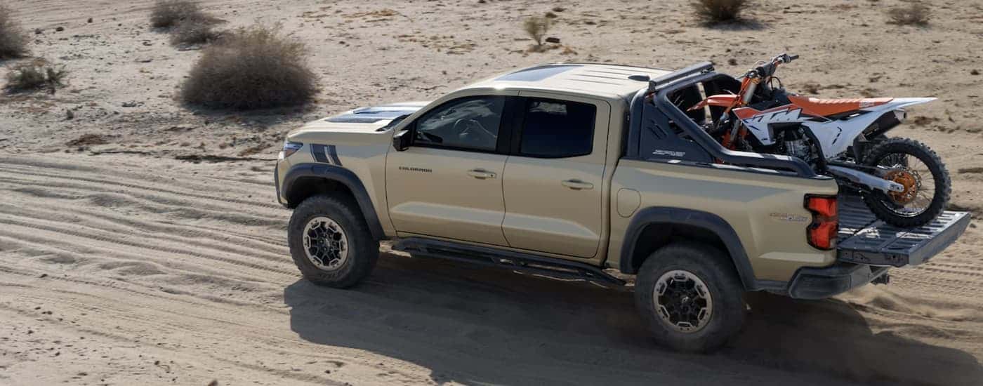 Rear angle view of a tan 2024 Chevy Colorado ZR2 Desert Boss driving in a desert.
