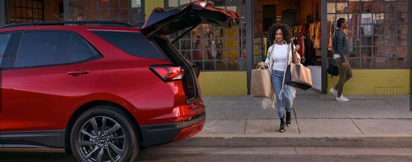 Woman bringing bags to a red 2024 Chevy Equinox RS with an open hatch.