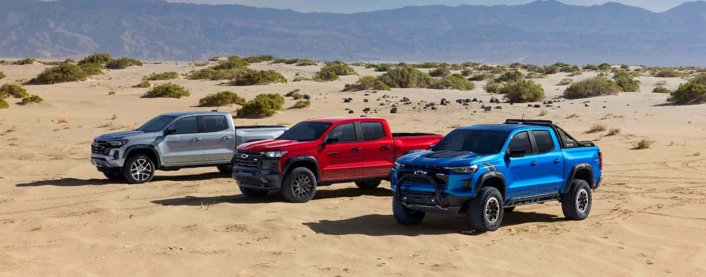 A silver 2023 Chevy Colorado Z71, a red Trail Boss, and a blue ZR2 Desert Boss are shown off-road.