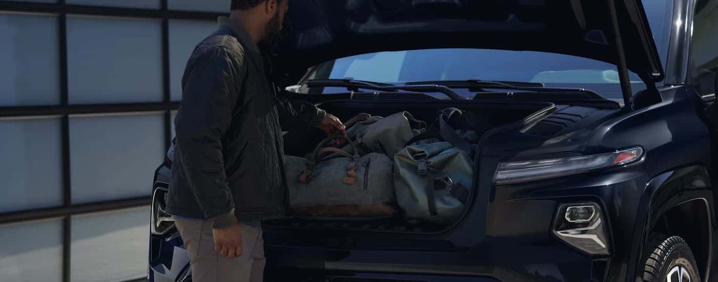 A man is getting bags out of the frunk of a black 2025 Chevy Silverado EV.