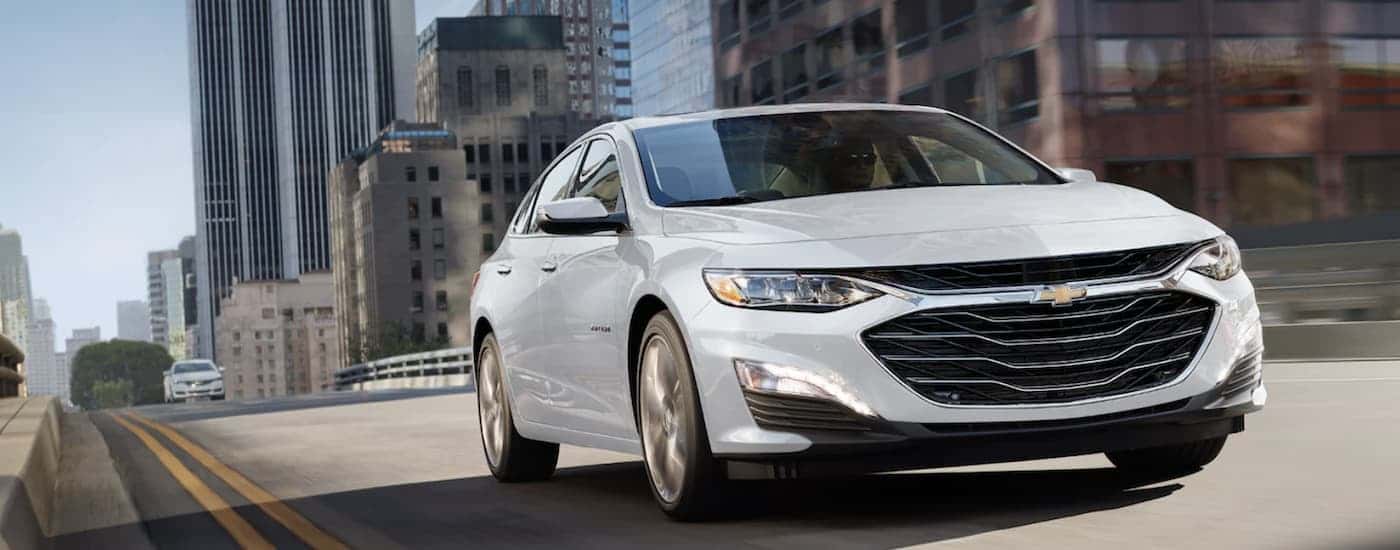 A white 2022 Chevy Malibu driving across a bridge from dealer with used cars.