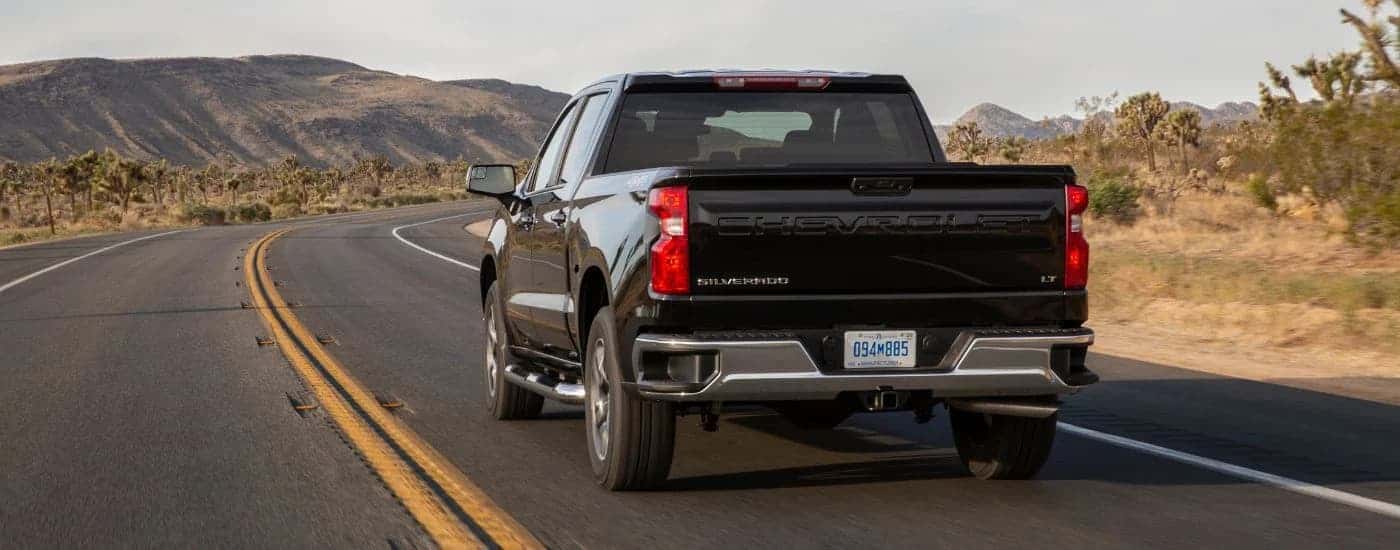 Rear view of a black 2022 Chevy Silverado 1500 LT driving down a desert road.