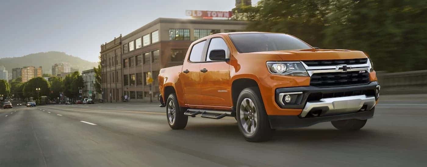 An orange 2021 Chevy Colorado Z71 driving from a dealer with used trucks for sale near Jersey Village.