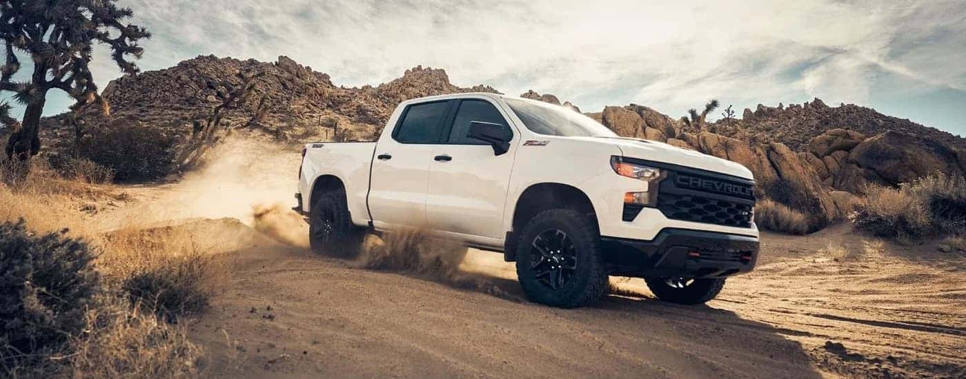 A white 2023 Chevy Silverado 1500 Z71 Trail Boss driving off-road down a desert hill.