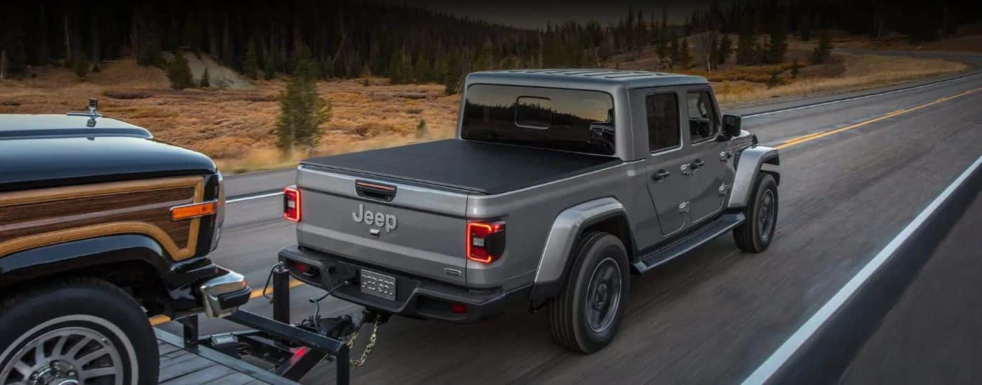 Rear view of a grey 2022 Jeep Gladiator towing a trailer down a road.
