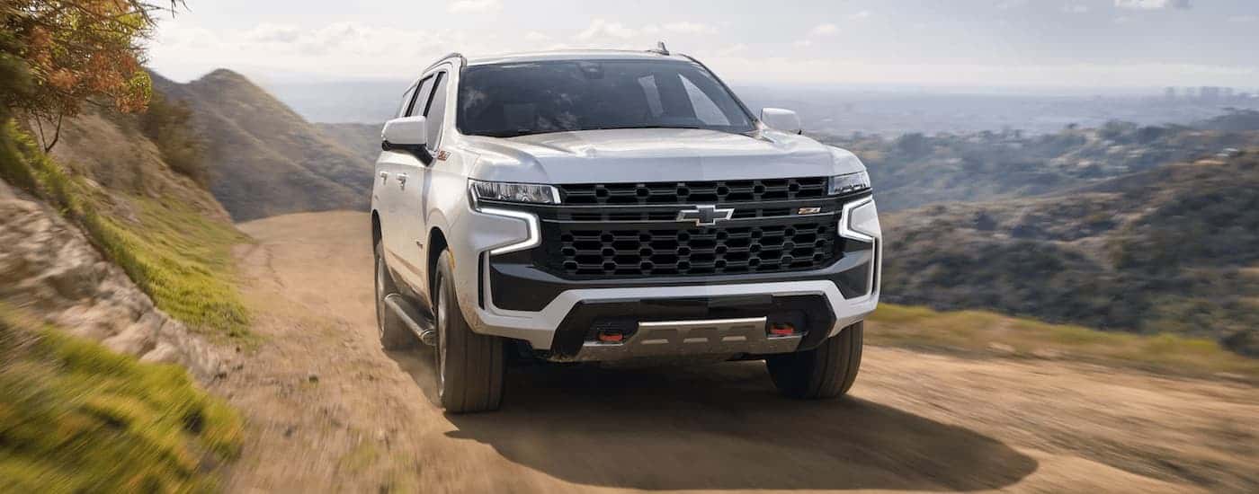 A white 2023 Chevy Tahoe Z71 is shown from a front angle driving on a dirt mountain road