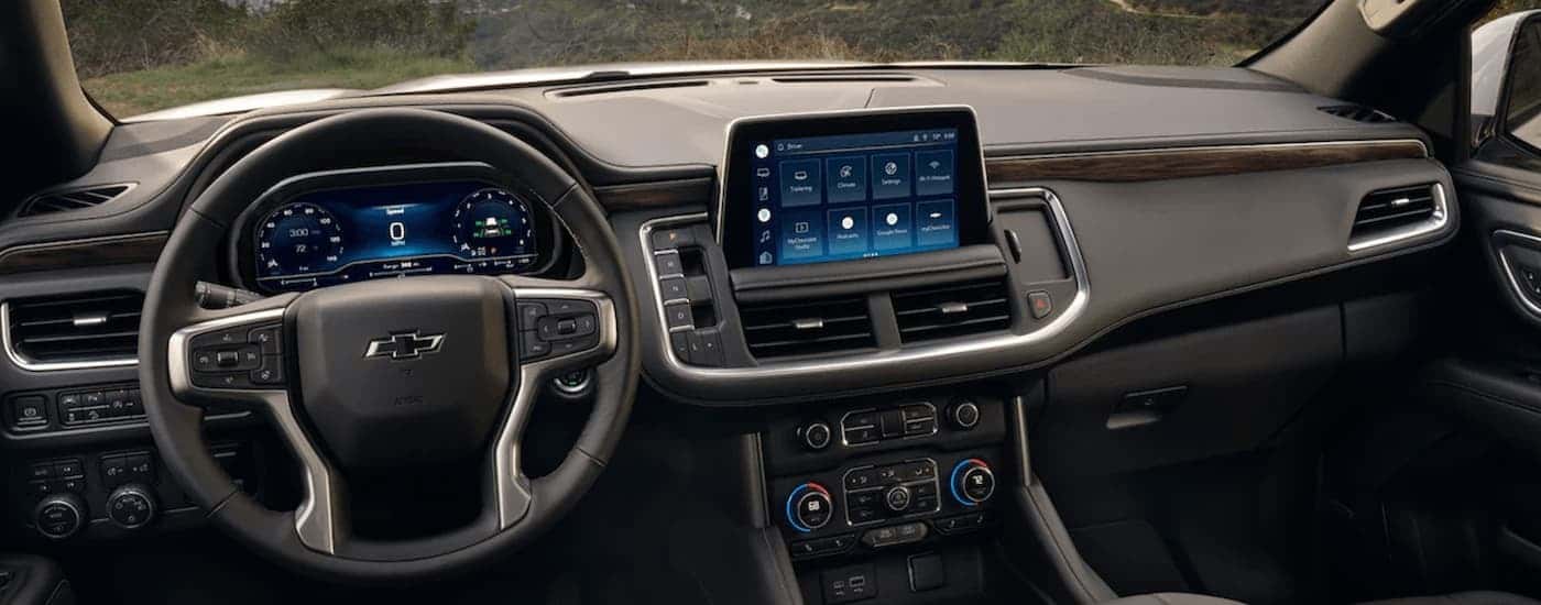 The black dashboard of a 2023 Chevy Tahoe for sale shows the steering wheel and infotainment screen
