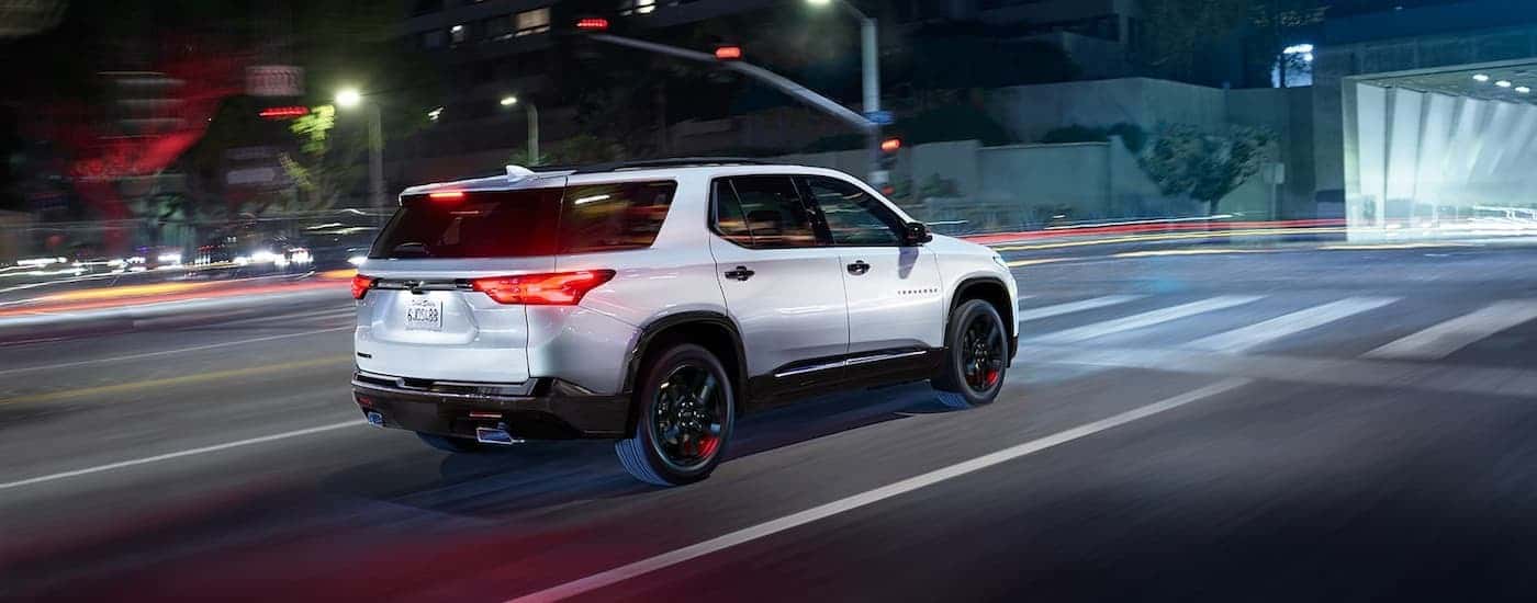 A white 2022 Chevy Traverse is shown from the rear driving through a city at night