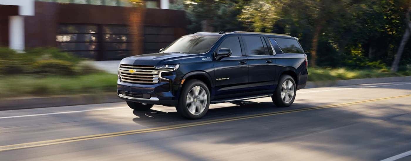A blue 2021 used Chevy Suburban for sale is shown driving on a city street