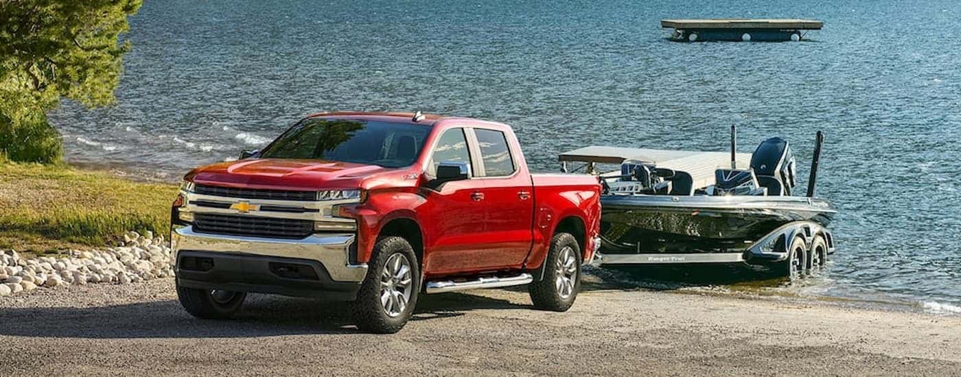 A red 2022 Chevy Silverado 1500 is shown towing a boat out of a lake